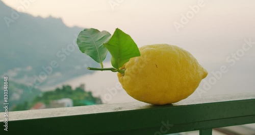 On a balcony railing, a ripe lemon rests with a backdrop of the Amalfi coast's sea and misty mountains. photo