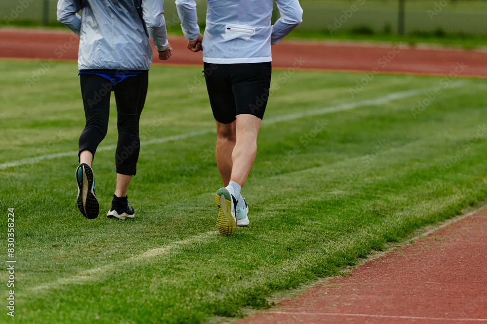 An inspiring and active elderly couple showcase their dedication to fitness as they running together on a lush green field, captured in a close-up shot of their legs in motion. An inspiring and active elderly couple showcase their dedication to fitness as they running together on a lush green field, captured in a close-up shot of their legs in motion.