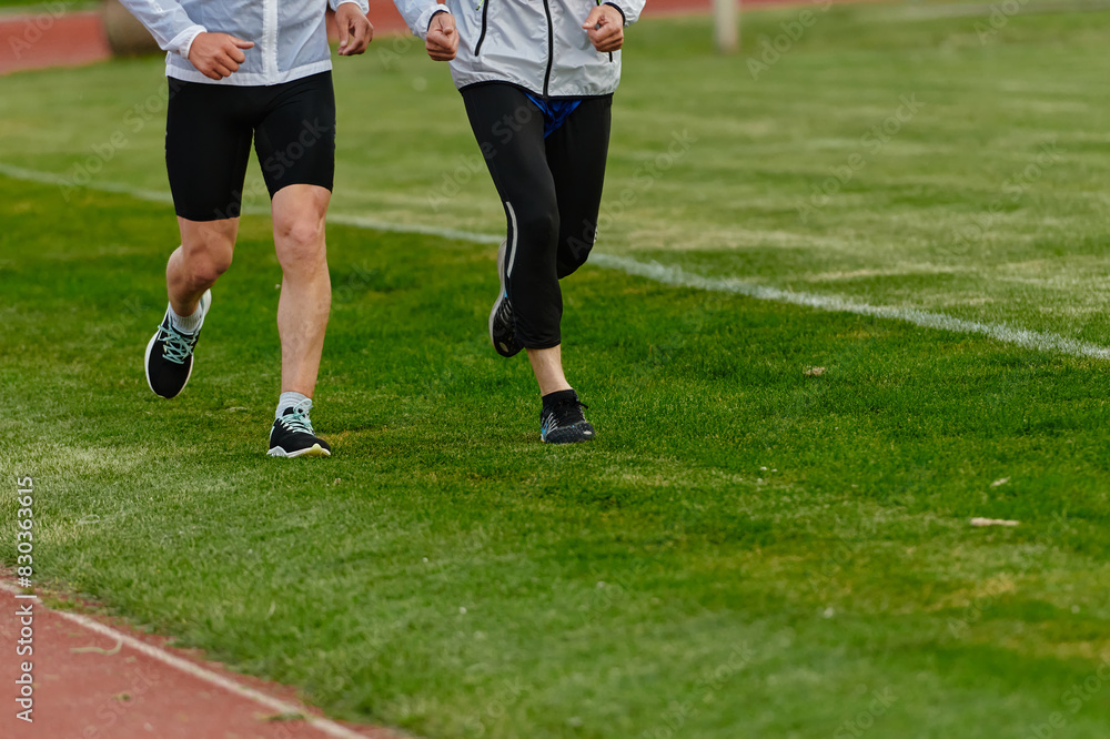 An inspiring and active elderly couple showcase their dedication to fitness as they running together on a lush green field, captured in a close-up shot of their legs in motion.