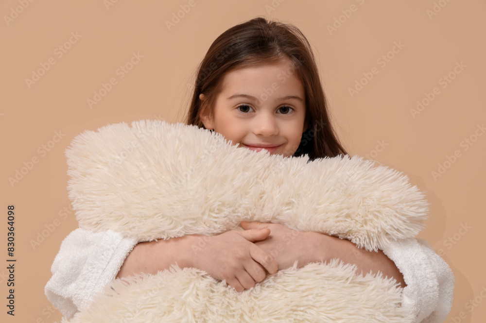 Cute little happy girl in bathrobe with pillow on beige background