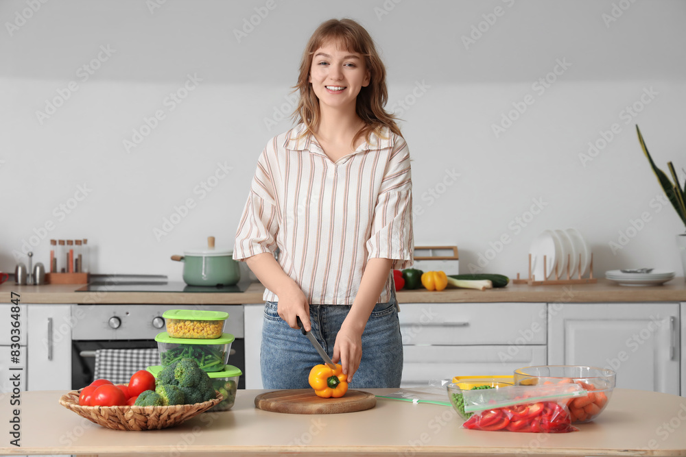 Young woman cutting bell pepper for freezing in kitchen