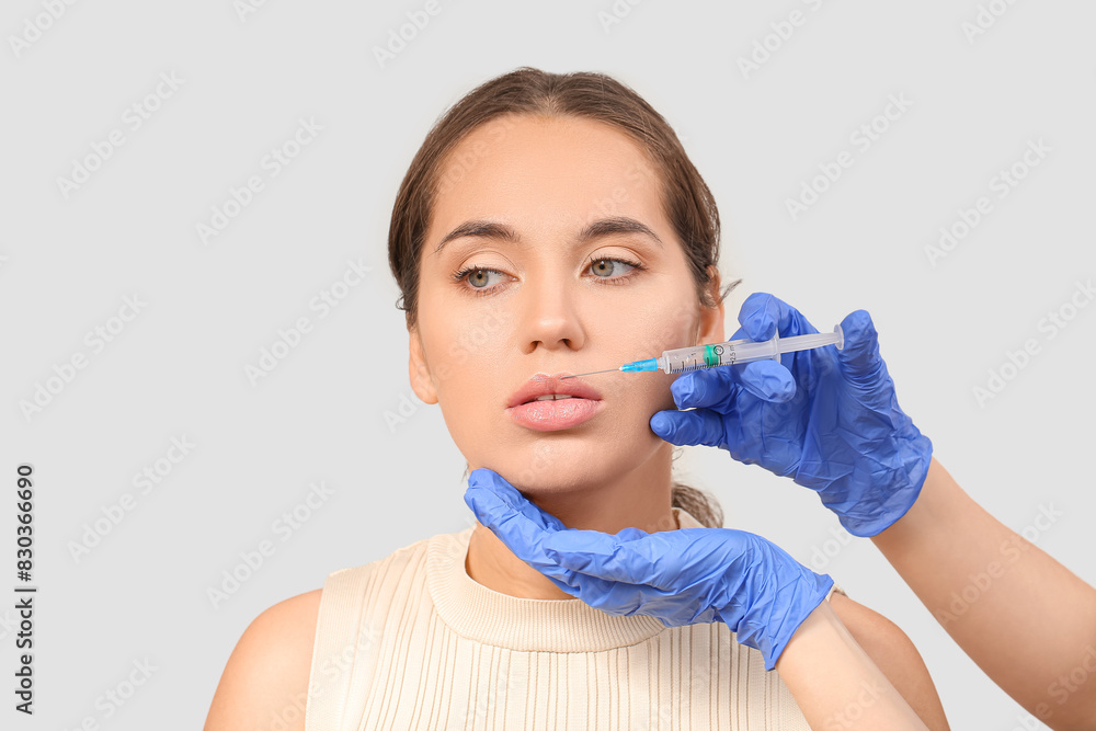Beautiful woman receiving lip injection on grey background