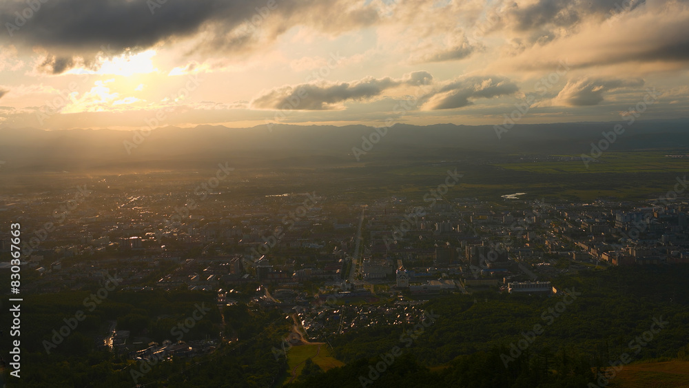 Top view of city in green valley with sun on horizon. Clip. Beautiful landscape of sunny green valley with town on summer day. Bright sun shines down on valley with town