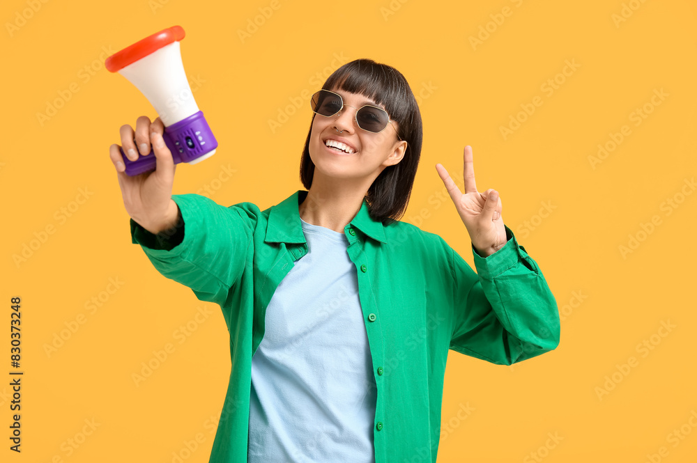 Young woman with megaphone showing victory gesture on yellow background Young woman with megaphone showing victory gesture on yellow background