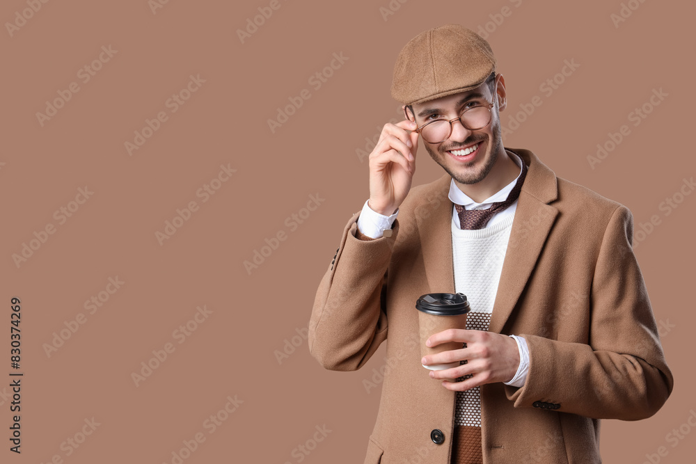 Handsome smiling young man in stylish coat with eyeglasses and paper cup of coffee posing on beige background Handsome smiling young man in stylish coat with eyeglasses and paper cup of coffee posing on beige background