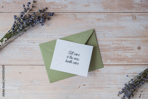 Paper card note with text SELF CARE IS THE NEW HEALTH CARE from green envelope. Lavender flower. Top view, flat lay. Concept of mental spiritual health self care wellbeing mindfulness photo