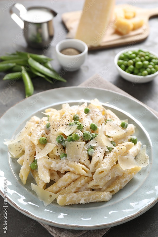 Delicious pasta with green peas, cheese, creamy sauce and ground pepper on grey table Delicious pasta with green peas, cheese, creamy sauce and ground pepper on grey table