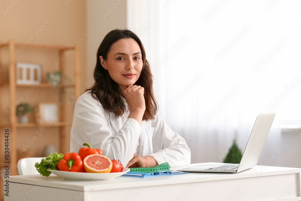 Young female nutritionist sitting at table in office