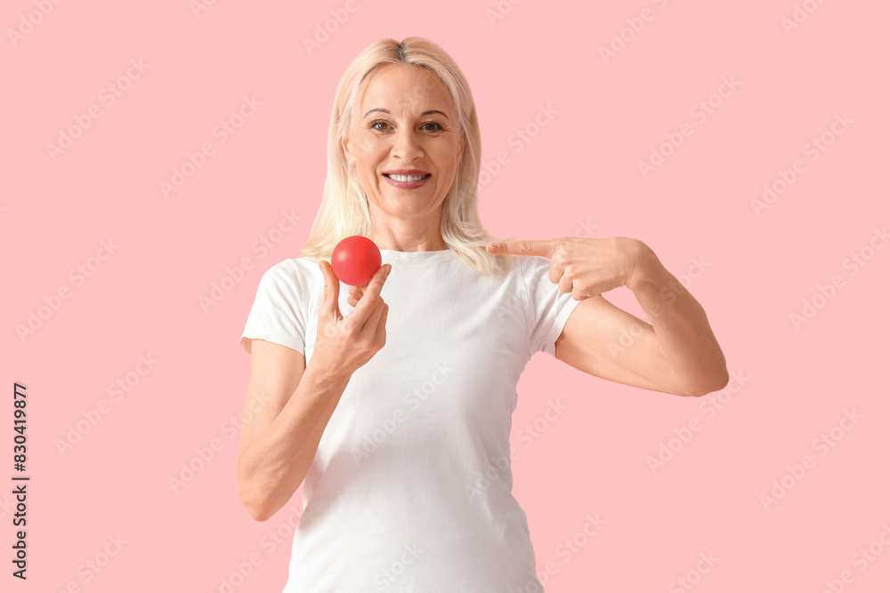 Mature woman pointing at massage ball on pink background Mature woman pointing at massage ball on pink background