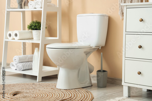 Interior of restroom with toilet bowl and furniture near beige wall