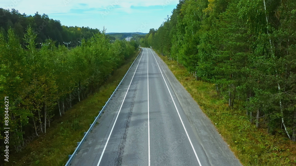 Flying over Scandinavian fir forest, crossing a country road. Footage. Aerial view of the empty road and summer forest.