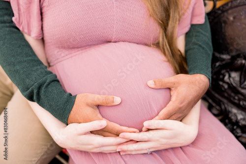 A man is cradling his pregnant wife's belly while they sit down. 