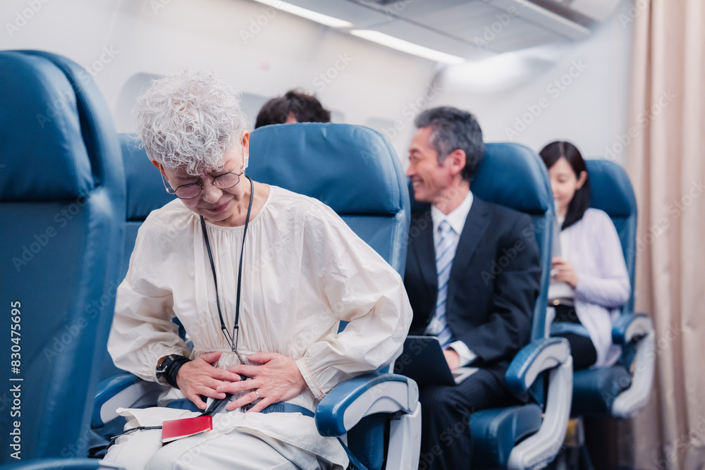 飛行機の機内で体調不良に苦しむ高齢の女性 飛行機の機内で体調不良に苦しむ高齢の女性