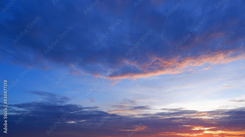 Obraz premium A stunning sunset with a gradient sky transitioning from deep blue at the top to warmer hues of orange and pink near the horizon. Clouds are illuminated with a golden glow. Sunset sky background. 