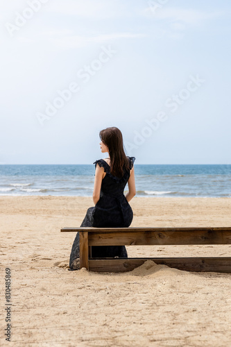 The inner woman in a black long dress is watching the sea by the seaside