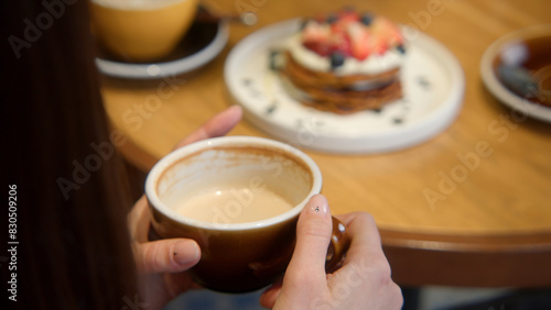 Fototapeta Naklejka Na Ścianę i Meble -  Close-up of beautiful woman having lunch in cafe with coffee and dessert. Stock footage. Woman drinks coffee with beautiful dessert in cafe. Beautiful aesthetic lunch with dessert and coffee in cafe