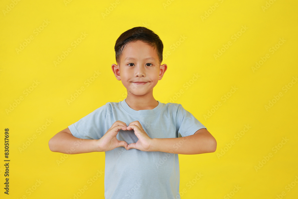 Smiling Asian little boy child with a heart shape symbol with hands isolated on yellow background. Smiling Asian little boy child with a heart shape symbol with hands isolated on yellow background.