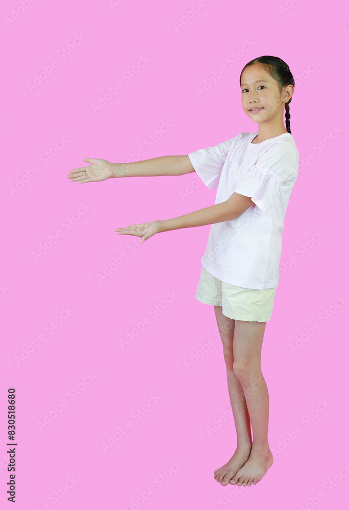 Smiling Asian girl child standing presenting something on copy space, isolated on pink studio background. Image full length with clipping path. Smiling Asian girl child standing presenting something on copy space, isolated on pink studio background. Image full length with clipping path.