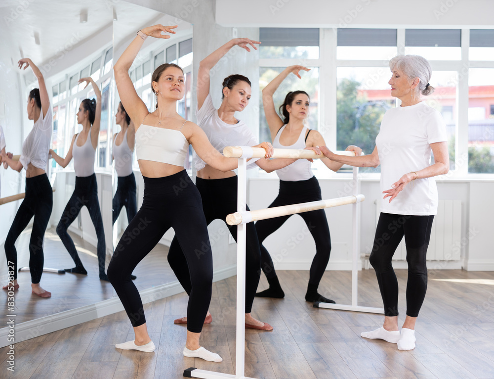 Experienced choreographer teaches ballet dancers movements at ballet barre in a choreographic studio