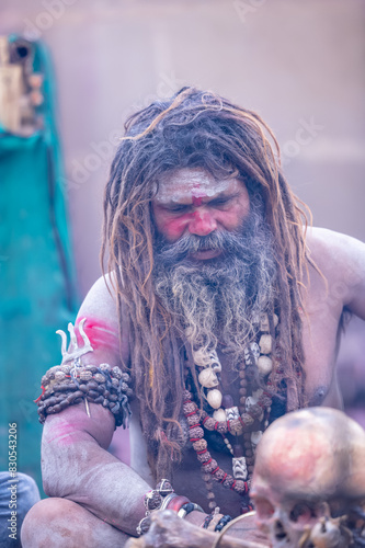 Portrait of an naga aghori sadhu holy man with pyre ash on his face and body performing aghor sadhna and smoking chilam at harishchandra ghat in varanasi.	
 photo