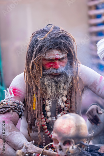 Portrait of an naga aghori sadhu holy man with pyre ash on his face and body performing aghor sadhna and smoking at harishchandra ghat in varanasi.	
