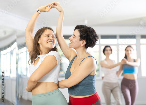 Two enthusiastic young women enjoying in brightly-lit dance studio, energetically moving to rhythm of salsa as dance partners.. © JackF