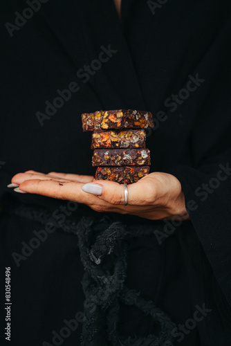 Female hands are holding chocolate bars mixed with nuts and fruits at black background