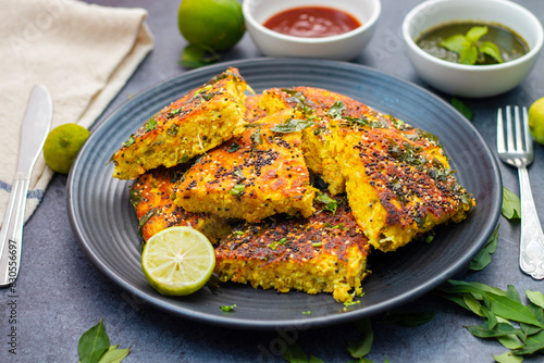 selective focus of Gujrati dish handvo slice tringle cut decorated with lemon, curry leaves, mint chutney and tomato sauce.