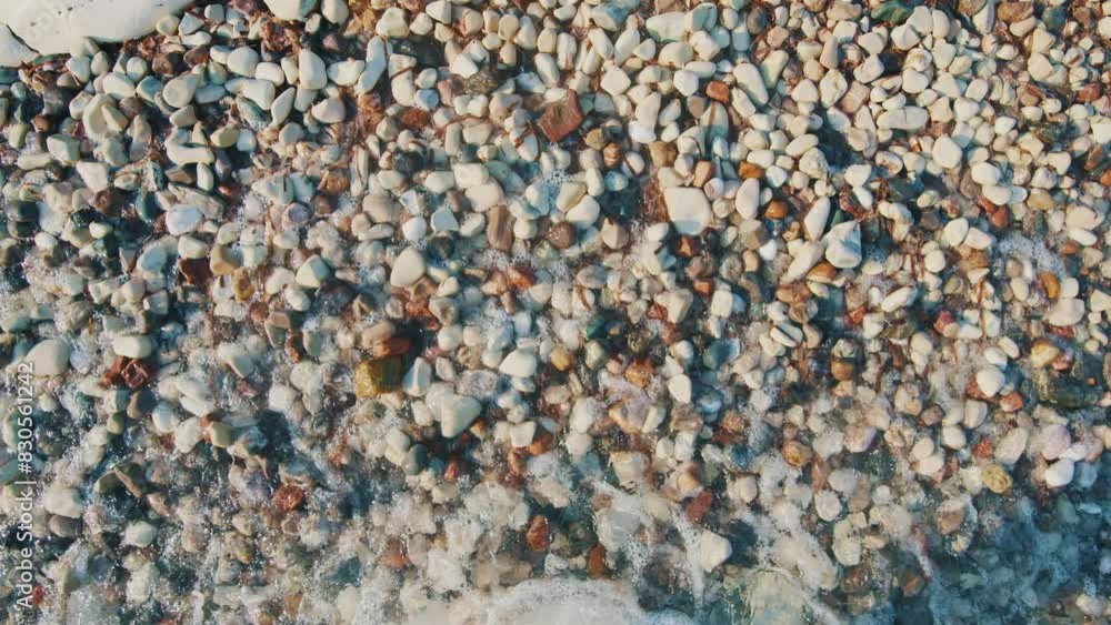 Waves gently crash against a pebbly shore, where countless stones of varying colors and sizes glisten under the sunlight. Waves gently crash against a pebbly shore, where countless stones of varying colors and sizes glisten under the sunlight.