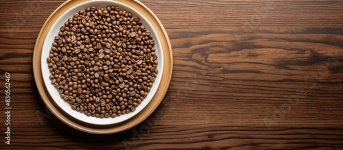 A top down view of a cluster of coffee seeds arranged on a bamboo plate surrounded by a wooden table with empty space for further items. Creative banner. Copyspace image