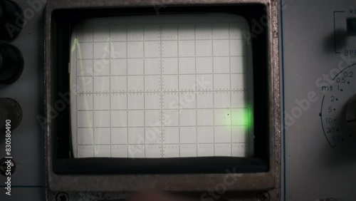 Hand adjusts knobs on a vintage oscilloscope, transforming the green waveforms displayed on the screen. This footage evokes the tactile nature of retro technology and the precision of signal analysis photo