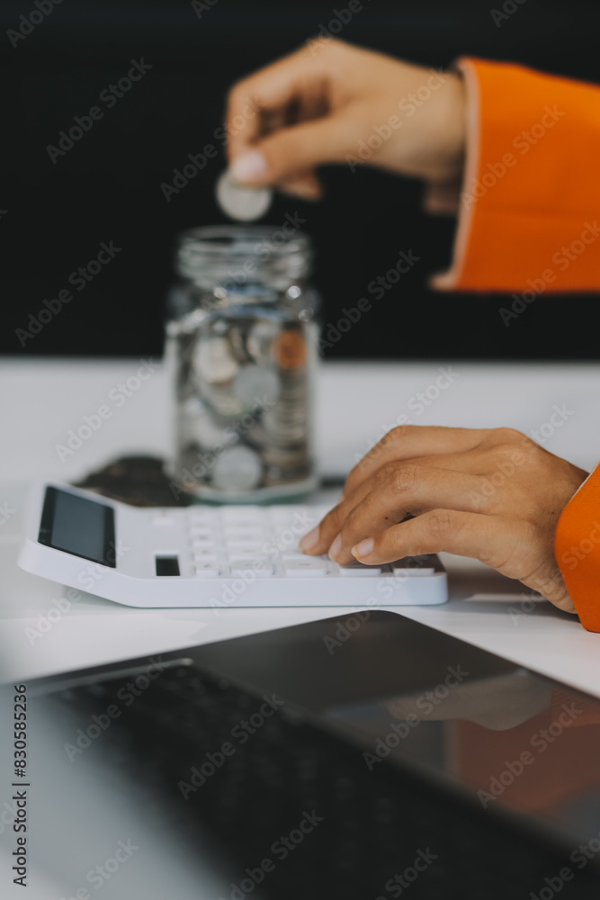Fototapeta premium Beautiful Asian businesswoman insert coins in a pin piggy bank on the table. saving money, investment, currency concept