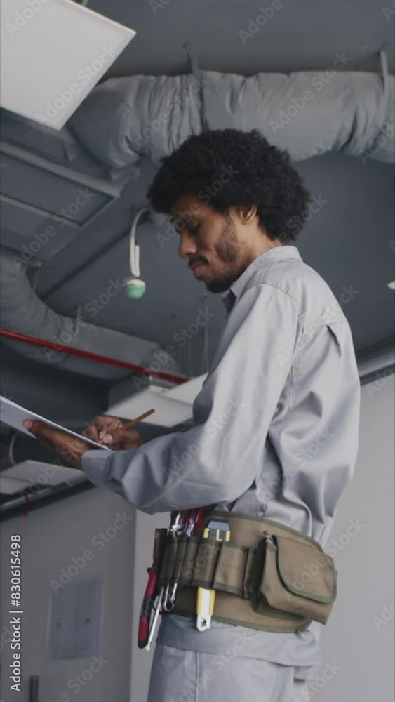 Vertical shot of African American construction worker writing information in cost sheet Vertical shot of African American construction worker writing information in cost sheet