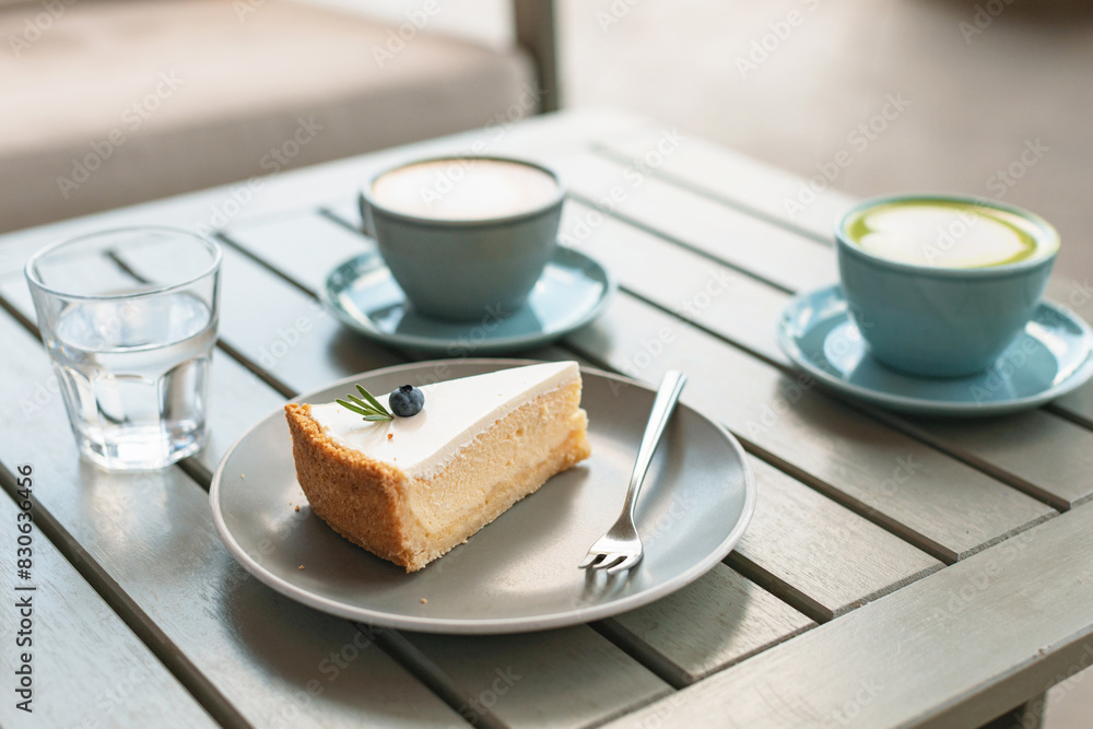 A piece of classic cheesecake decorated with a berry and rosemary on a plate, hot drinks on the table on the terrace. A piece of classic cheesecake decorated with a berry and rosemary on a plate, hot drinks on the table on the terrace.