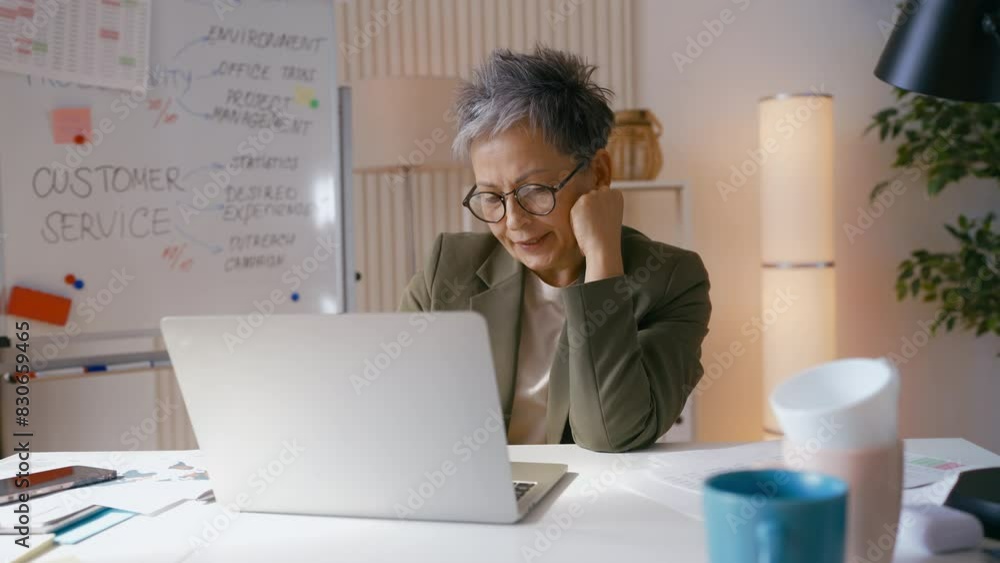 Grey-haired female employee yawning while working on laptop, feeling bored Grey-haired female employee yawning while working on laptop, feeling bored
