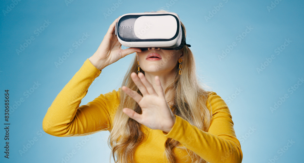 VR, woman and hand in studio for metaverse, digital and video game on blue background. Technology, virtual and streaming for gamer person, hobby and internet for 3d augmented reality experience VR, woman and hand in studio for metaverse, digital and video game on blue background. Technology, virtual and streaming for gamer person, hobby and internet for 3d augmented reality experience