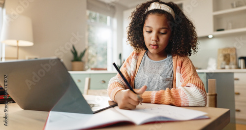 Girl child, education and writing with laptop for online learning in home, digital application and literature for growth or development. Kid, internet and virtual class for homeschooling and website. photo