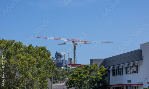 A tower crane erected to help in the construction of a new commercial building in an urban area with trees on the Gold Coast in Queensland, Australia with a blue sky background. photo