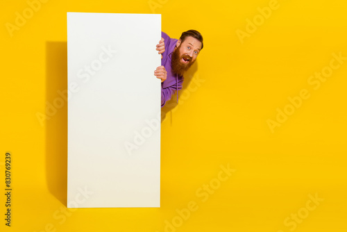 Full length photo of funky positive man peeking behind empty space big screen isolated on yellow color background