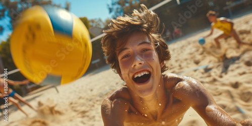 Male teen volleyball player catching the ball on a beach on a sunny day. Teenage friends playing beach volleyball together. Active leisure for kids.
