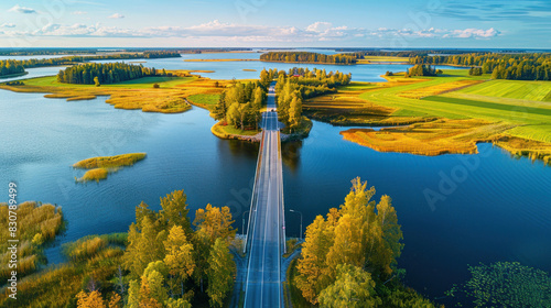 Beautiful aerial vista of a bridge crossing a tranquil blue lake, with expansive green and yellow fields stretching out on either side in the Finnish countryside. photo
