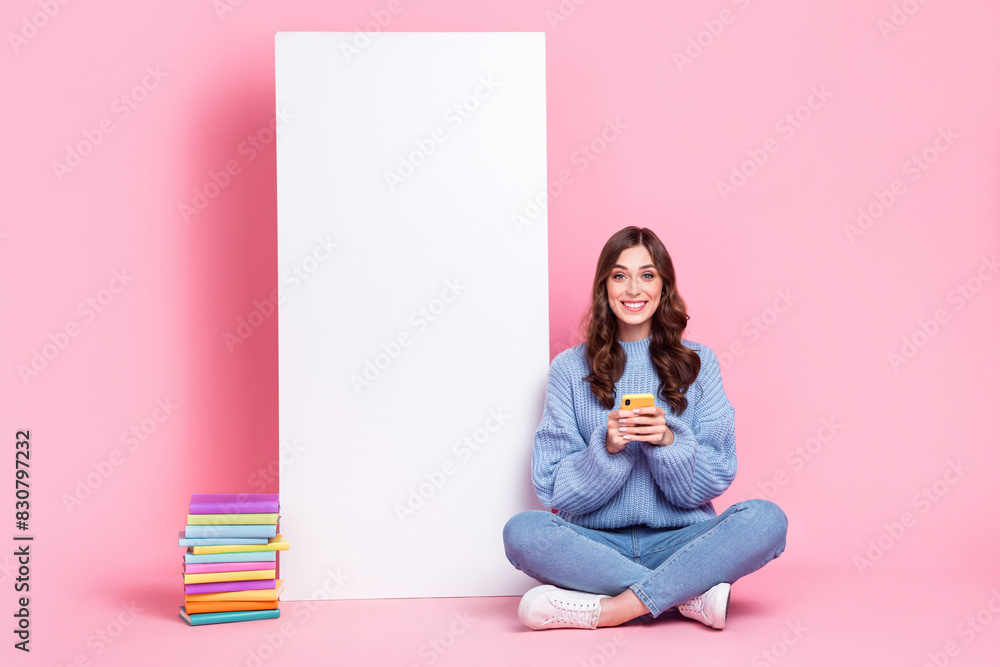 Full size portrait of positive cheerful girl sit floor use telephone big empty space display ad isolated on pink color background Full size portrait of positive cheerful girl sit floor use telephone big empty space display ad isolated on pink color background