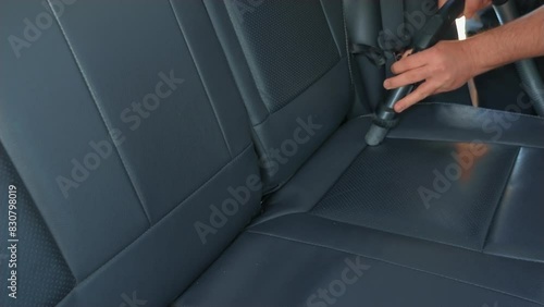 Car service worker uses vacuum cleaner. Close up hands man using hoover to clean dirty leather seats auto interior. Details of vacuum cleaning in car photo