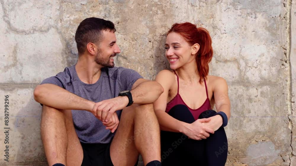 Sporty young couple smiling taking a break sitting talking while exercising outdoors. Sporty young couple smiling taking a break sitting talking while exercising outdoors.