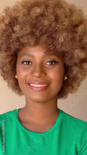 Happy young black woman with African style hair wearing green t-shirt looking at camera and smiling.  vertical video footage. stylish light makeup, pearl earrings photo
