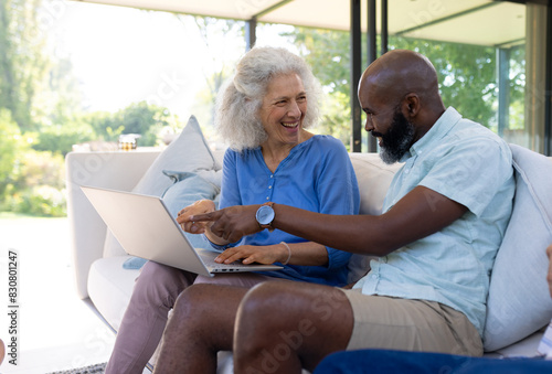 At home, diverse senior friends laughing while viewing laptop