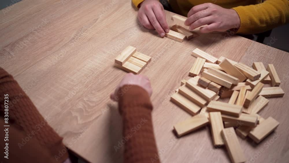 Hands stacking wooden blocks, playing a jenga game that demands strategy, skill, and concentration.