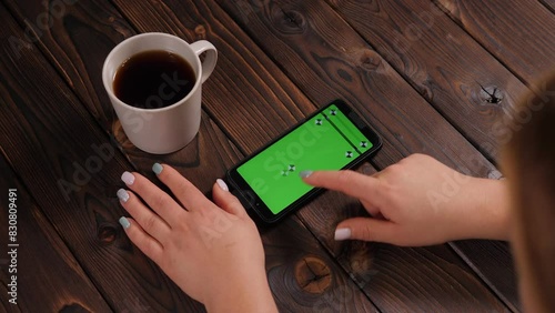 Close-up of a woman using a smartphone with a green screen sitting in a cafe, she drinks tea or coffee. Chromakey. Top view.