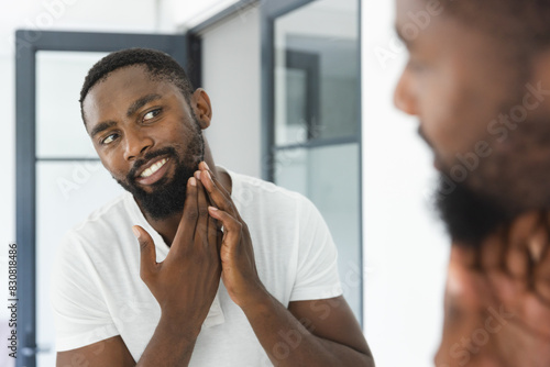 At home in bathroom, African American man checking his beard in mirror photo