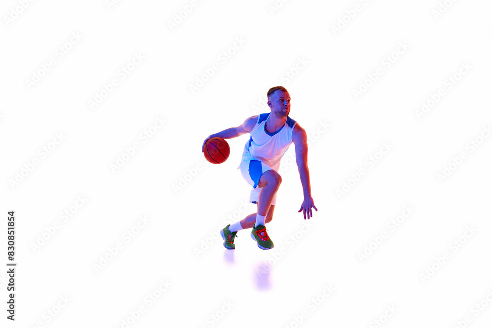 Action shot of young athletic man, basketball player controls ball showing balance and focus in neon light against white studio background. Concept of professional sport, games, tournament, action. Ad Action shot of young athletic man, basketball player controls ball showing balance and focus in neon light against white studio background. Concept of professional sport, games, tournament, action. Ad